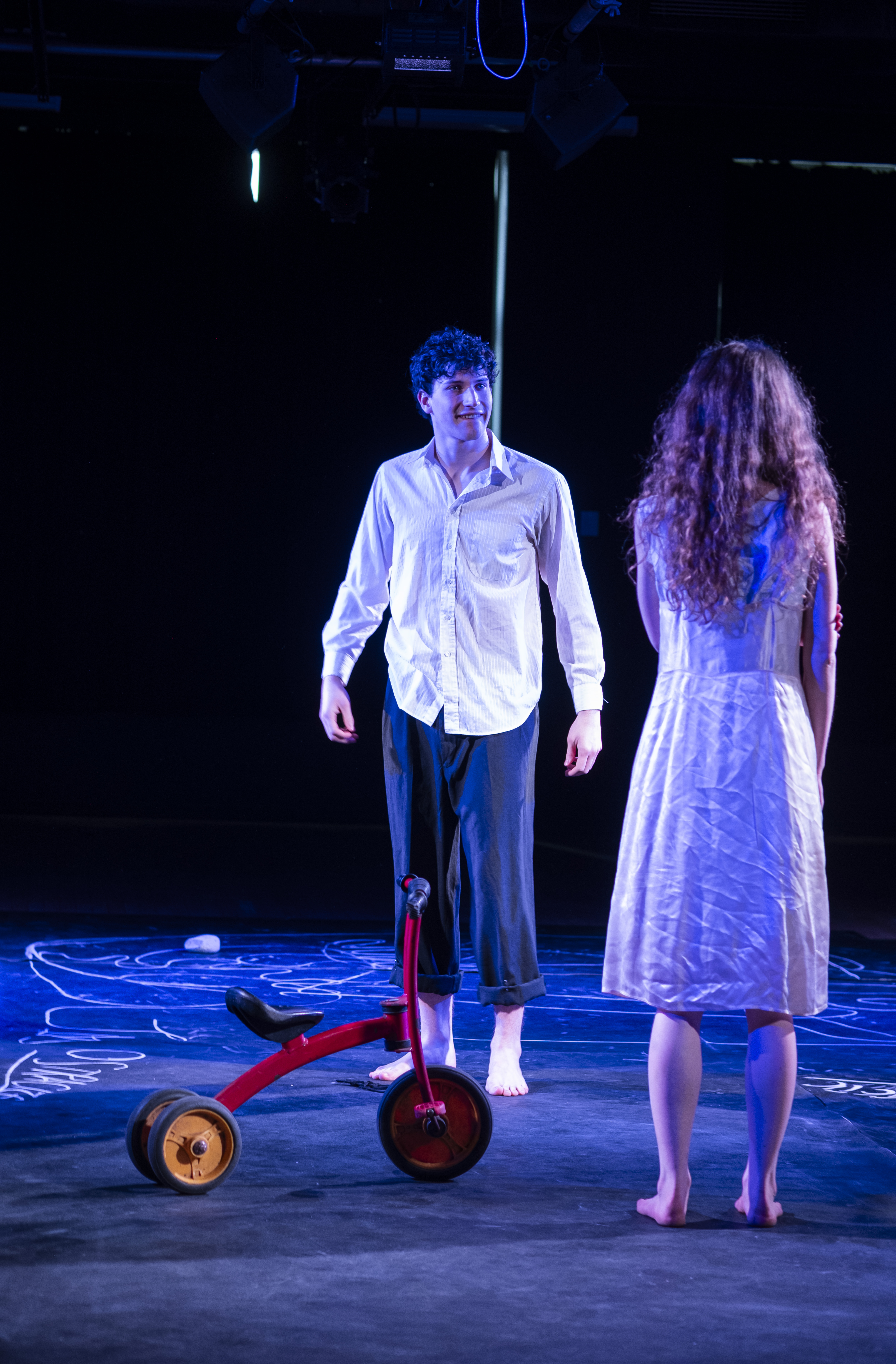 Two figures facing each other beside a red tricycle on the chalk floor.