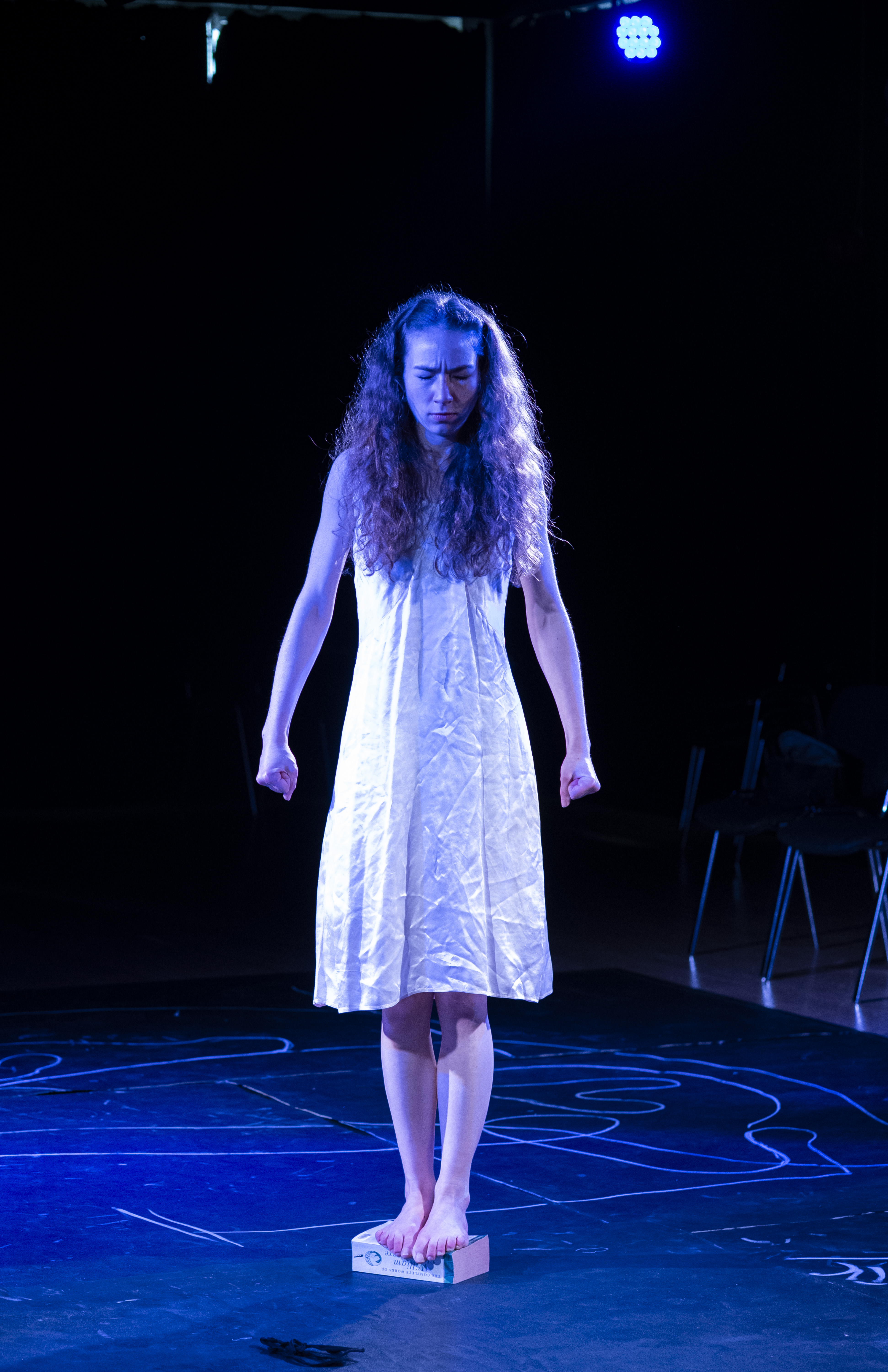 Eurydice in a white dress standing on a small block in blue light.
