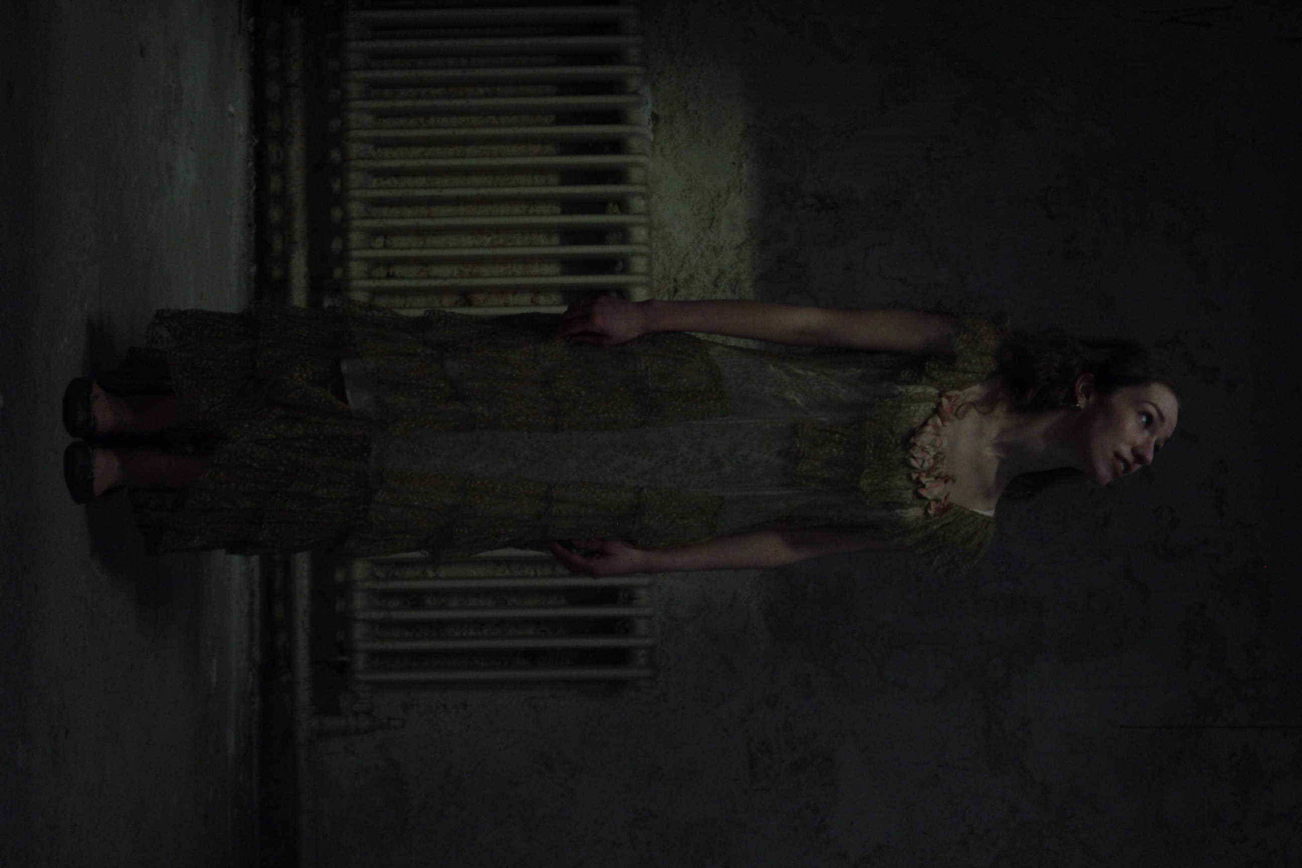 Promotional shot of Eurydice in her gown stretched along a radiator.