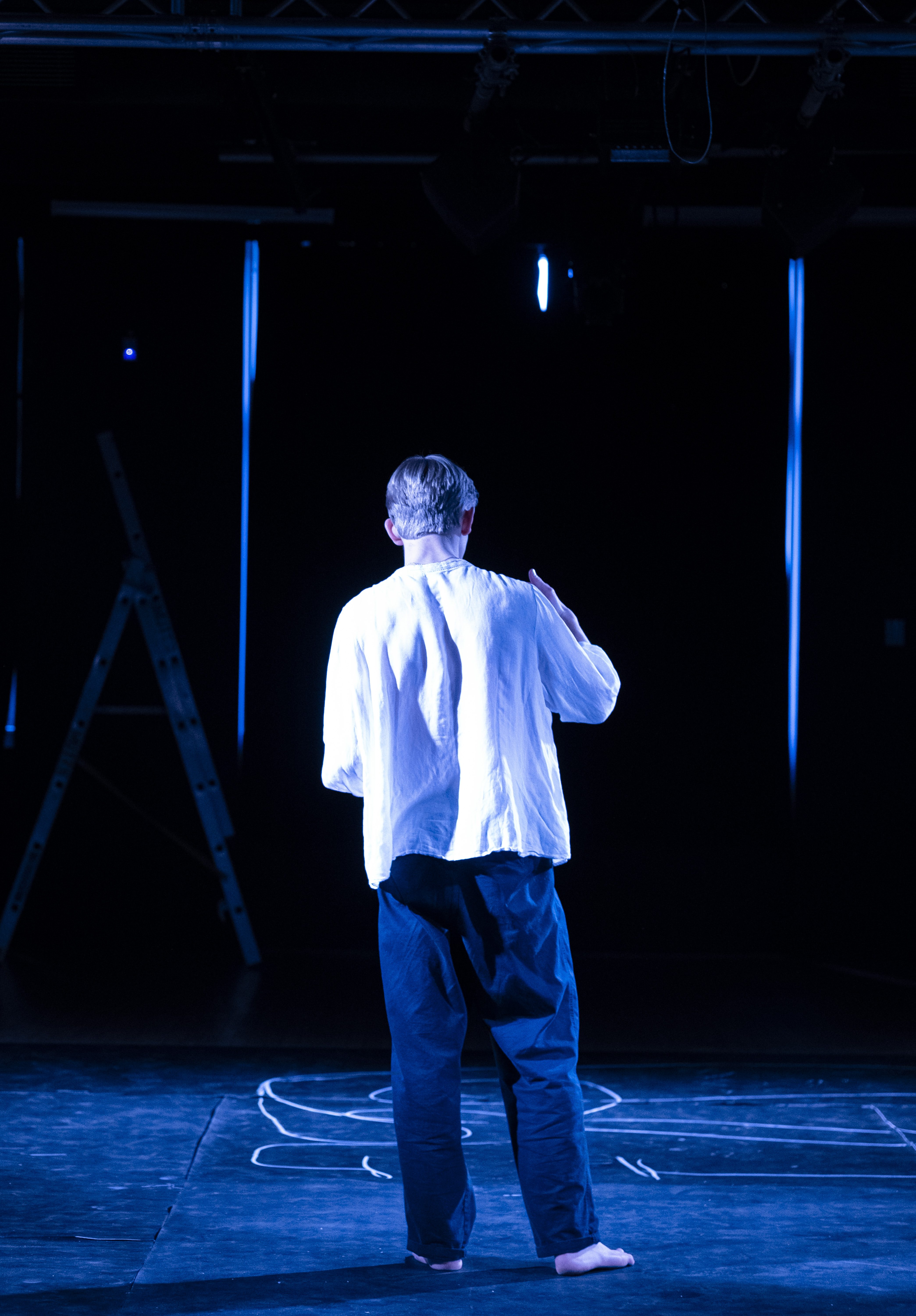 Orpheus alone with his back to the audience on the chalk-marked floor.