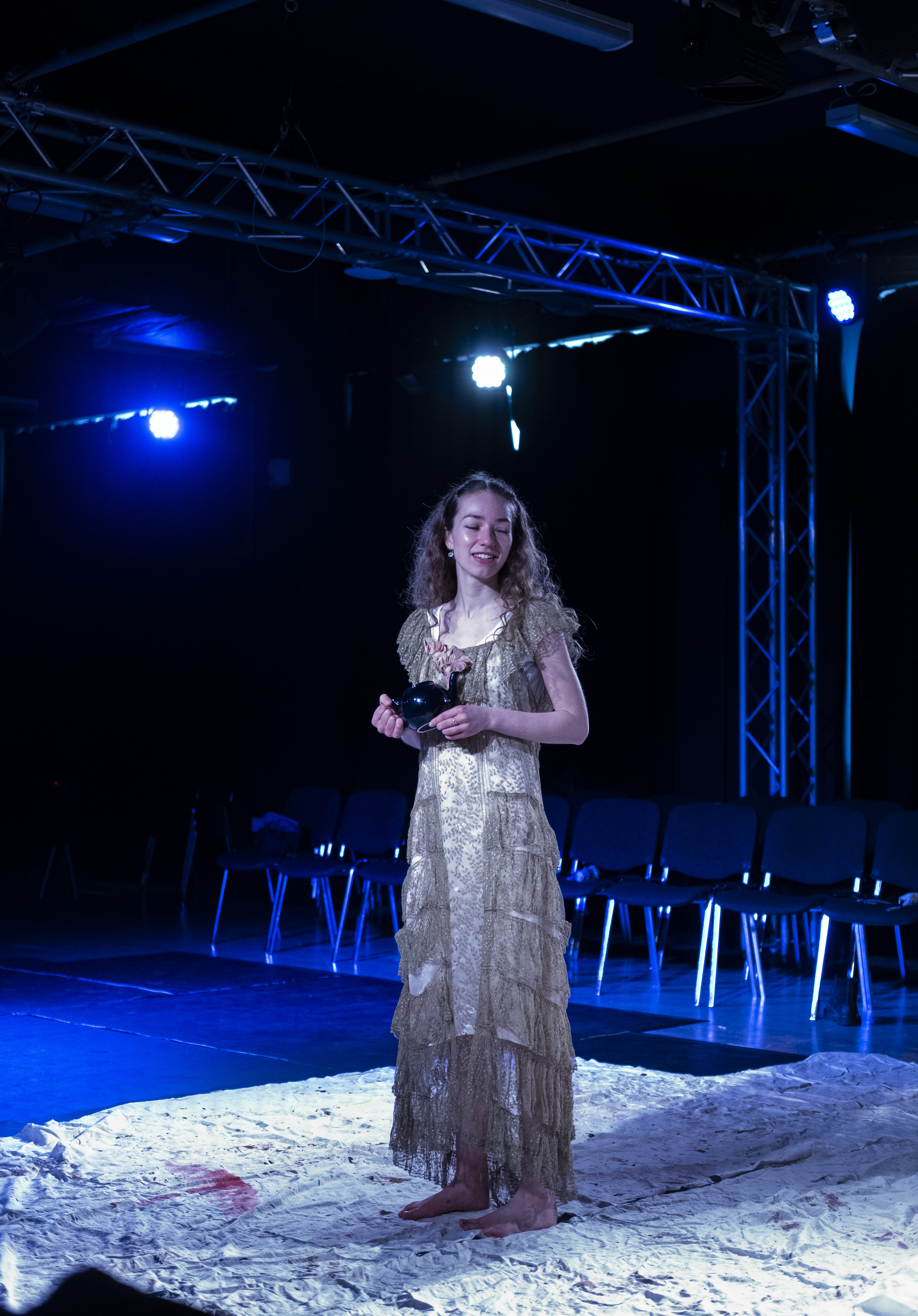 Eurydice alone in a gold gown under a blue wash, empty seats behind her.