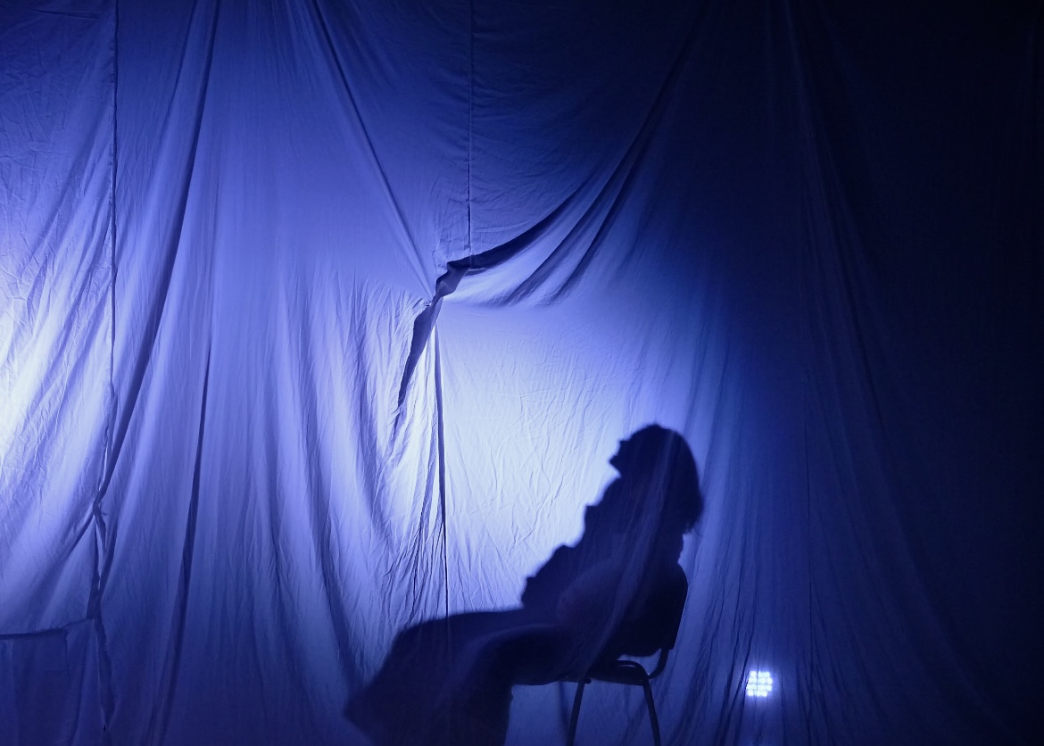 An empty chair casting a long shadow across the blue-lit drapes.