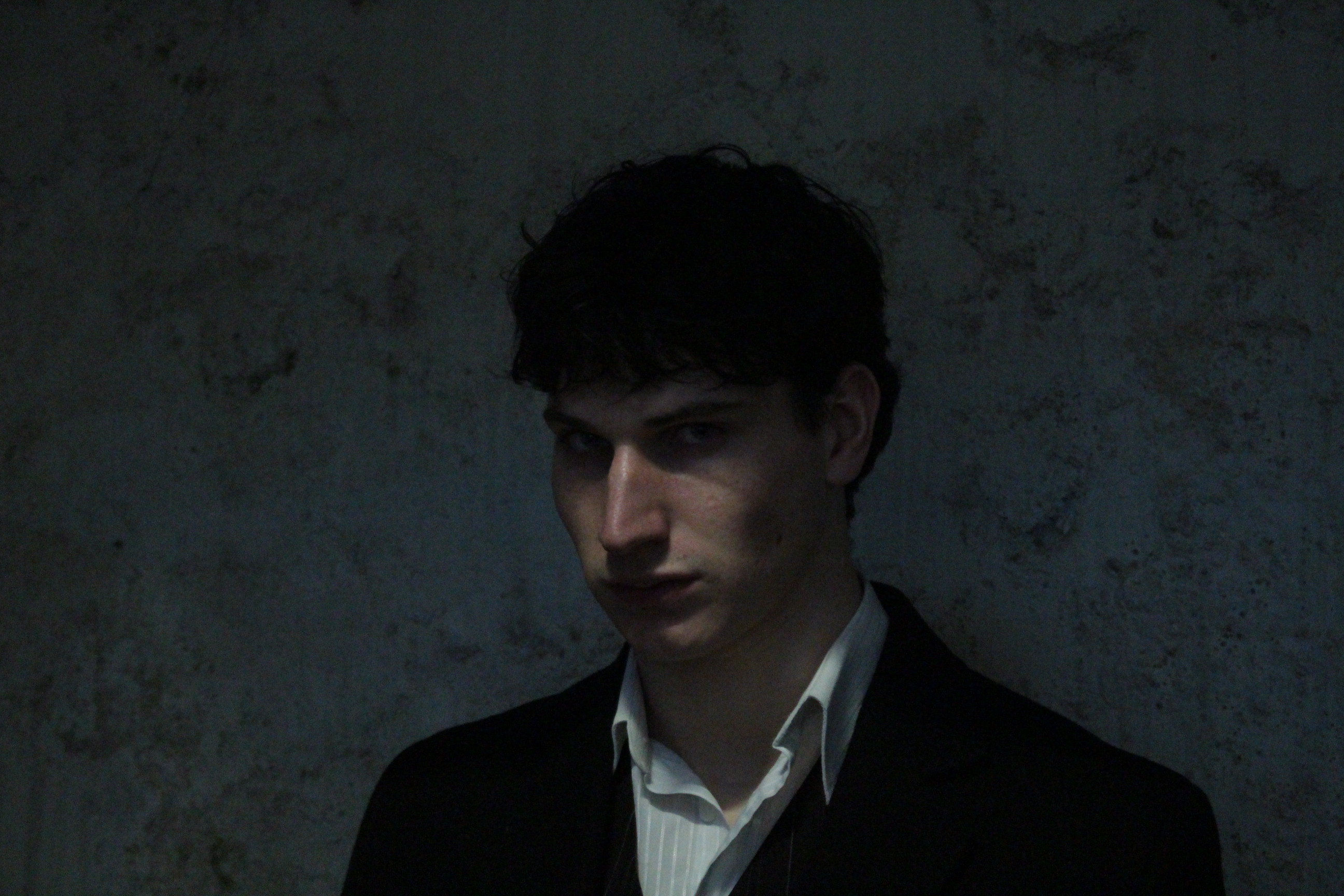 Promotional portrait, head turned to the side in low light.
