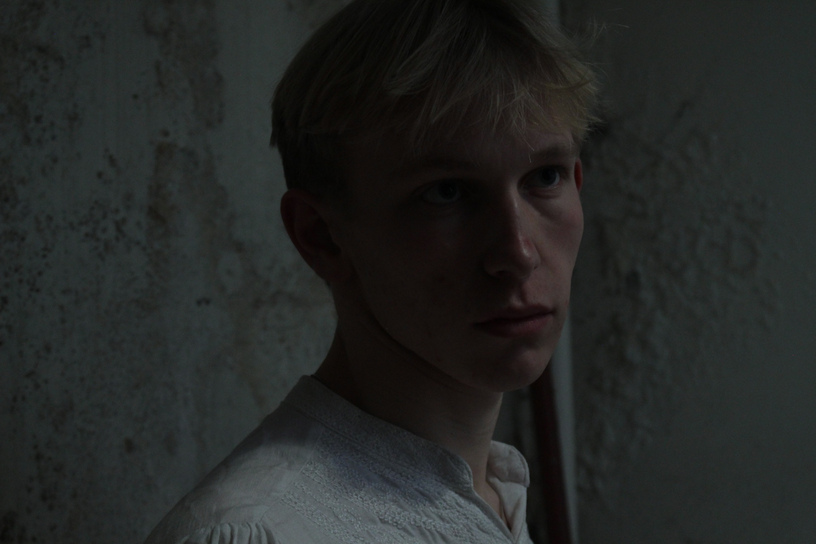 Promotional portrait of Orpheus against a bare plaster wall.