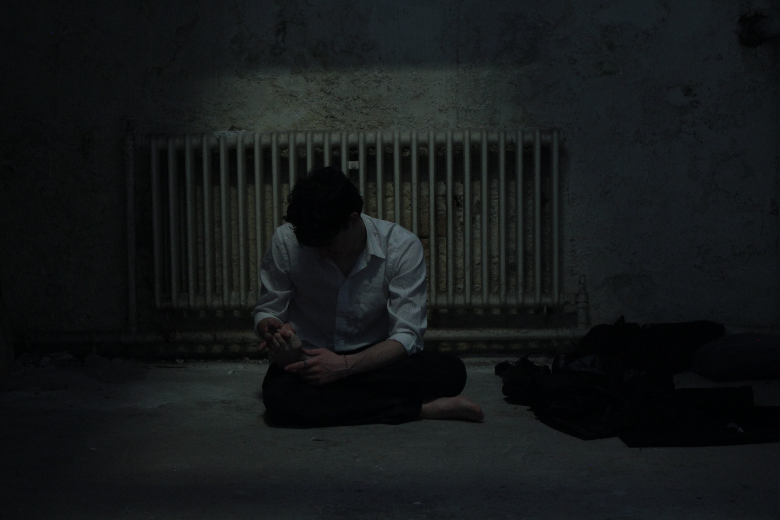 Promotional shot of a figure sitting on the floor beside a radiator.
