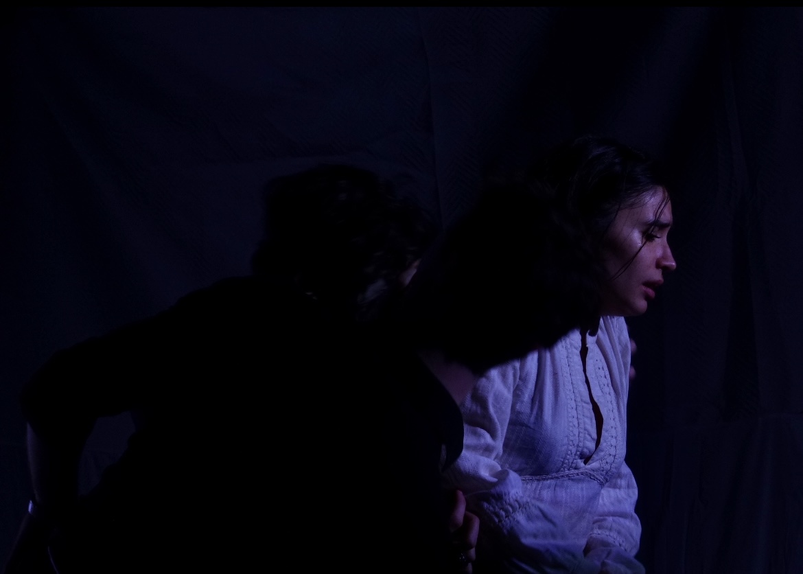 The Duchess in profile with a figure pressed close behind her in near darkness.