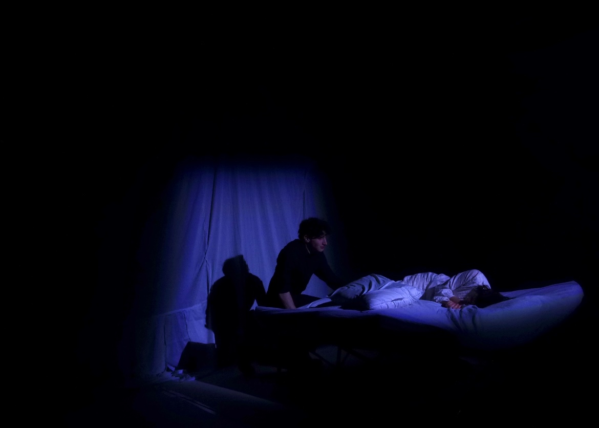 Bosola over the Duchess's bed, near-black stage with a single lamp.