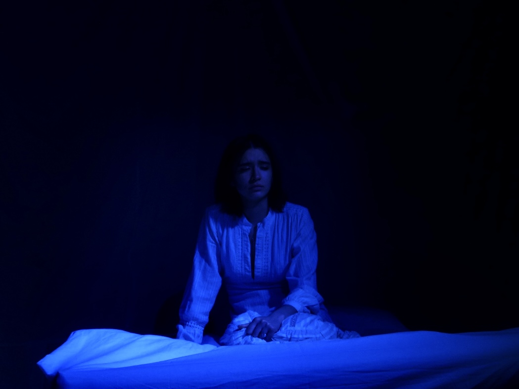 The Duchess sitting alone on the edge of her bed in dim blue light.