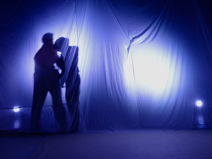 A silhouetted figure hauling back a white sheet in blue backlight.